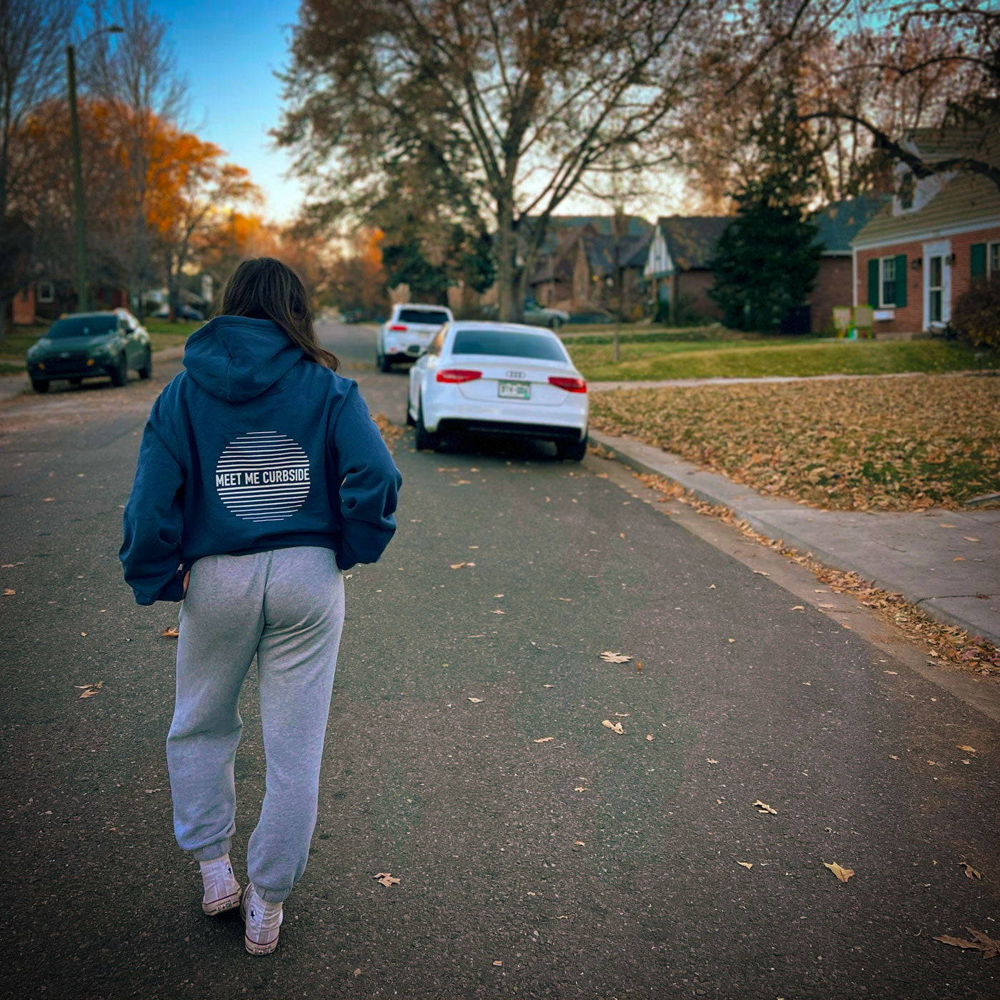 Teen girl walking down the street with oversized navy blue hoodie with cool graphic on back saying meet me curbside