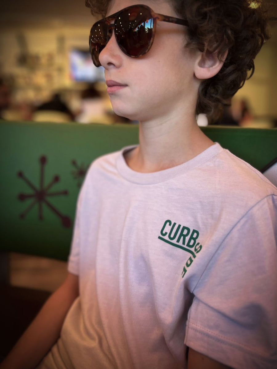 close up of teen boy with sunglasses, smirking wearing a soft, comfortable t shirt with curbside logo on pocket